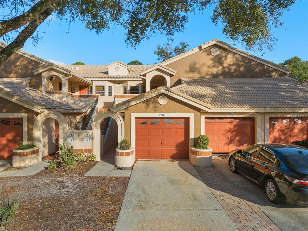 A row of tan stucco townhomes with orange garage doors and tiled roofs — 7784 SUGAR BEND DRIVE UNIT 7784, ORLANDO, FL