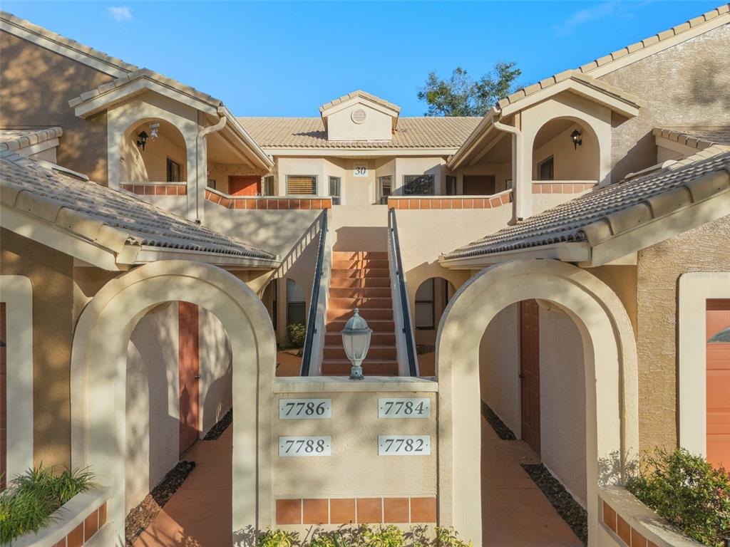 An exterior view of a two-story apartment building with arched entryways and central stairs — 7784 SUGAR BEND DRIVE UNIT 7784, ORLANDO, FL