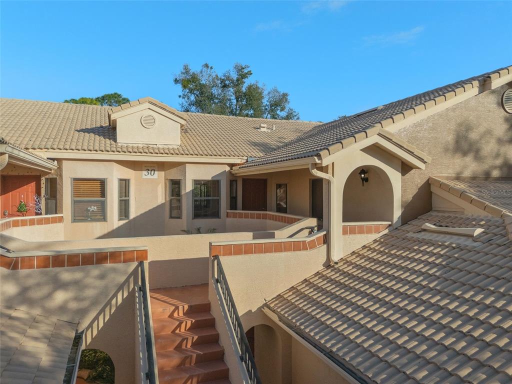 An exterior view of a multi-story stucco building with tiled roofs and an outdoor staircase — 7784 SUGAR BEND DRIVE UNIT 7784, ORLANDO, FL