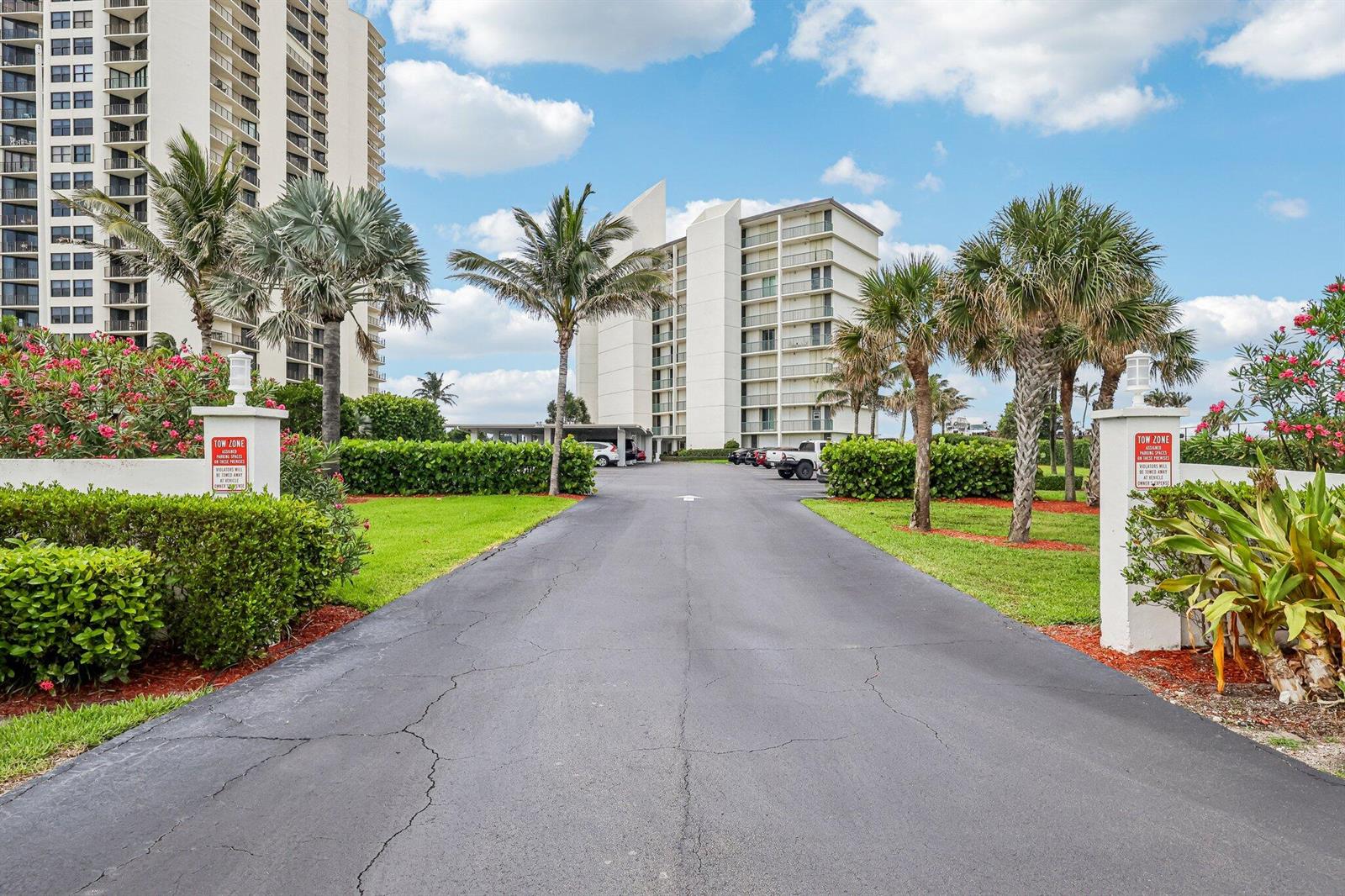 An asphalt driveway leads toward a tall white apartment building flanked by palm trees — 5400 N Ocean Drive E, Singer Island FL 33404, SINGER ISLAND, FL