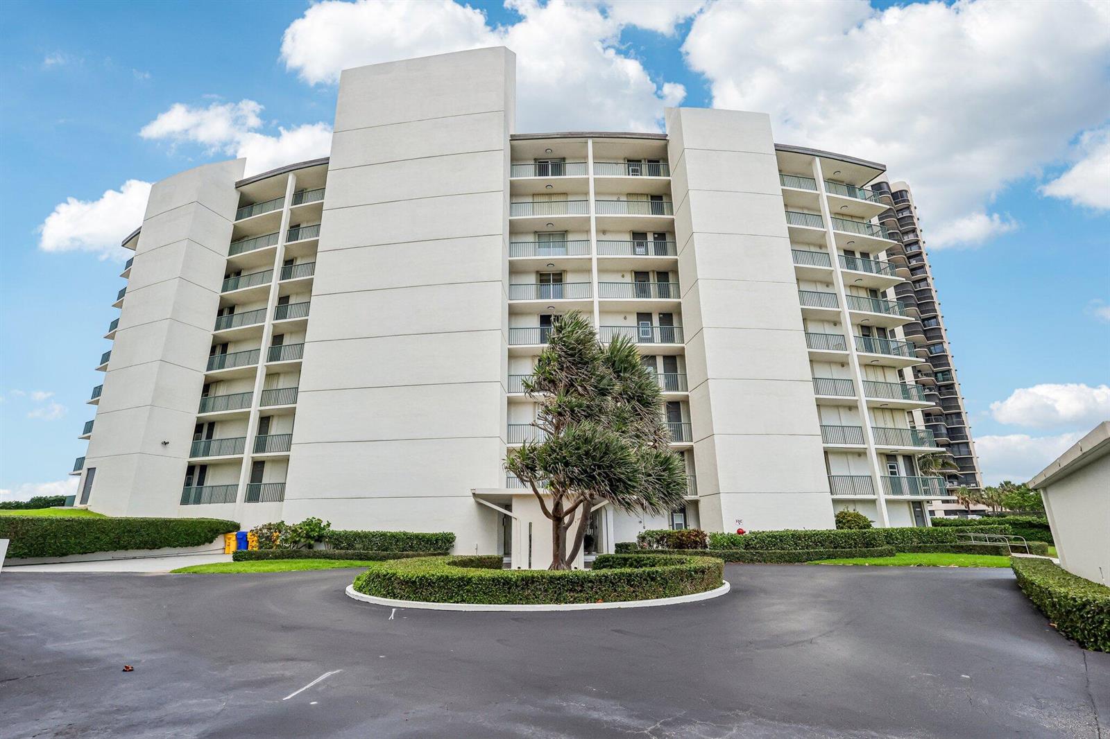 A multi-story white apartment building features balconies and a circular driveway with landscaping — 5400 N Ocean Drive E, Singer Island FL 33404, SINGER ISLAND, FL