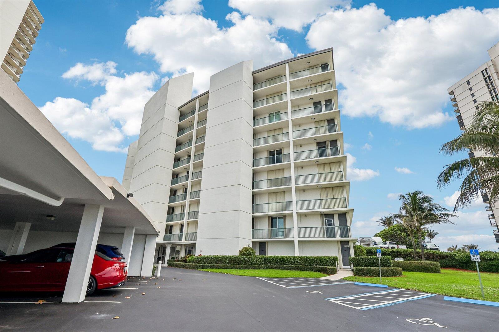 A multi-story white apartment building with balconies stands next to a covered parking area — 5400 N Ocean Drive E, Singer Island FL 33404, SINGER ISLAND, FL