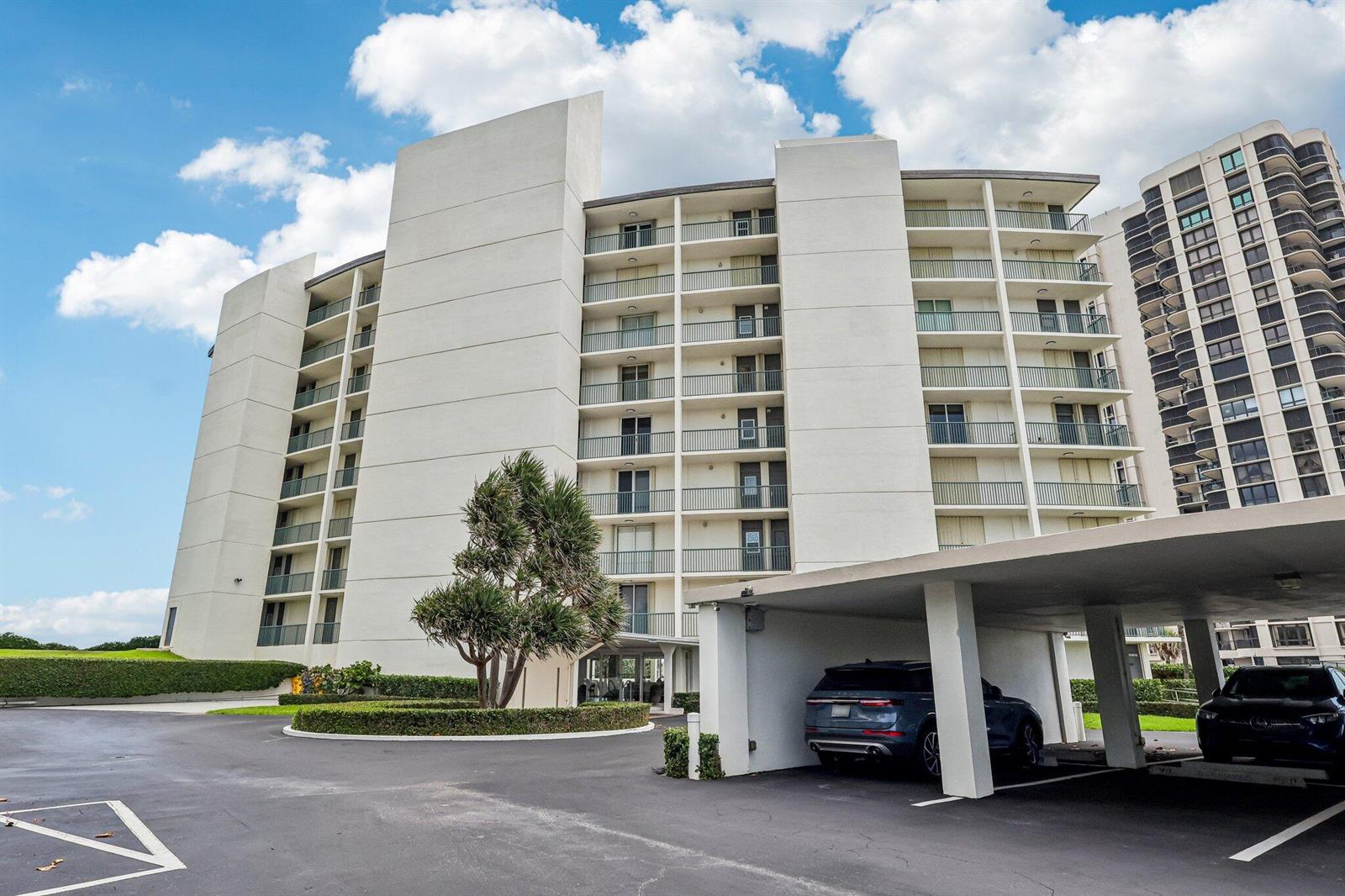 A multi-story white apartment building features balconies and a covered parking area with cars — 5400 N Ocean Drive E, Singer Island FL 33404, SINGER ISLAND, FL