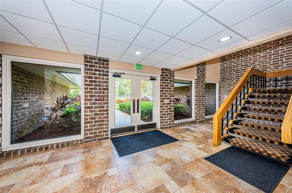An indoor entryway features tile flooring, brick walls, a glass exit door, and a staircase — 36750 US HIGHWAY 19 N UNIT 5-104, PALM HARBOR, FL