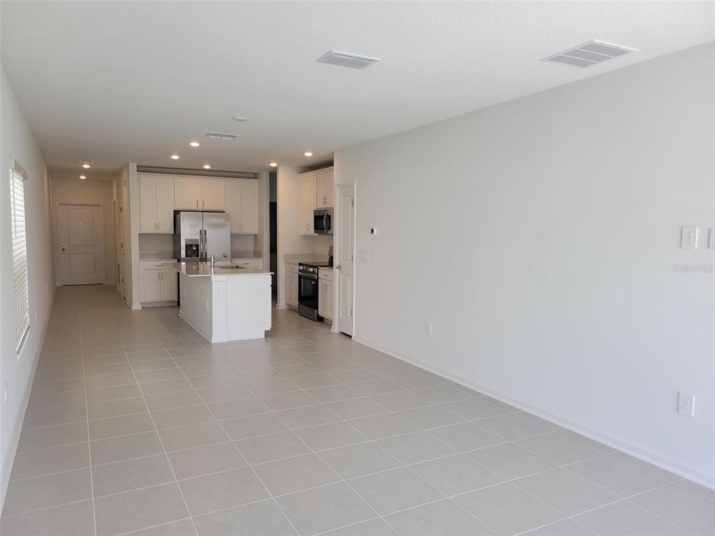 An open-concept kitchen with white cabinetry and an island overlooks a large, tiled living area — 5635 VINYASA ROAD, CLERMONT, FL