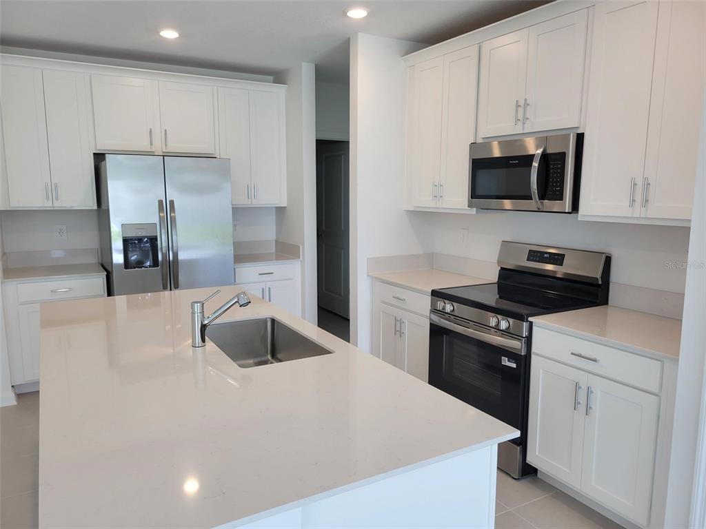 A modern kitchen features white cabinets, stainless steel appliances, and a large quartz-topped island — 5635 VINYASA ROAD, CLERMONT, FL