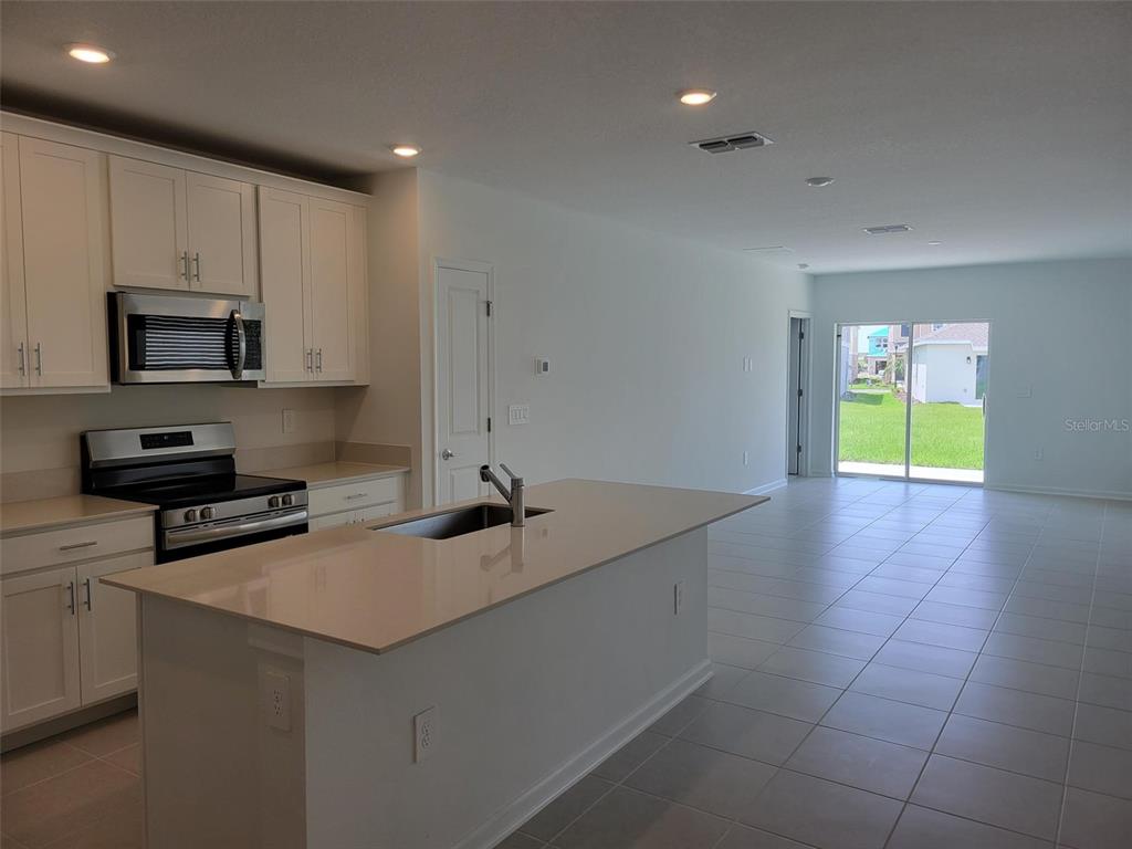 A kitchen with white cabinets, stainless steel appliances, and a central island overlooks a living area — 5635 VINYASA ROAD, CLERMONT, FL