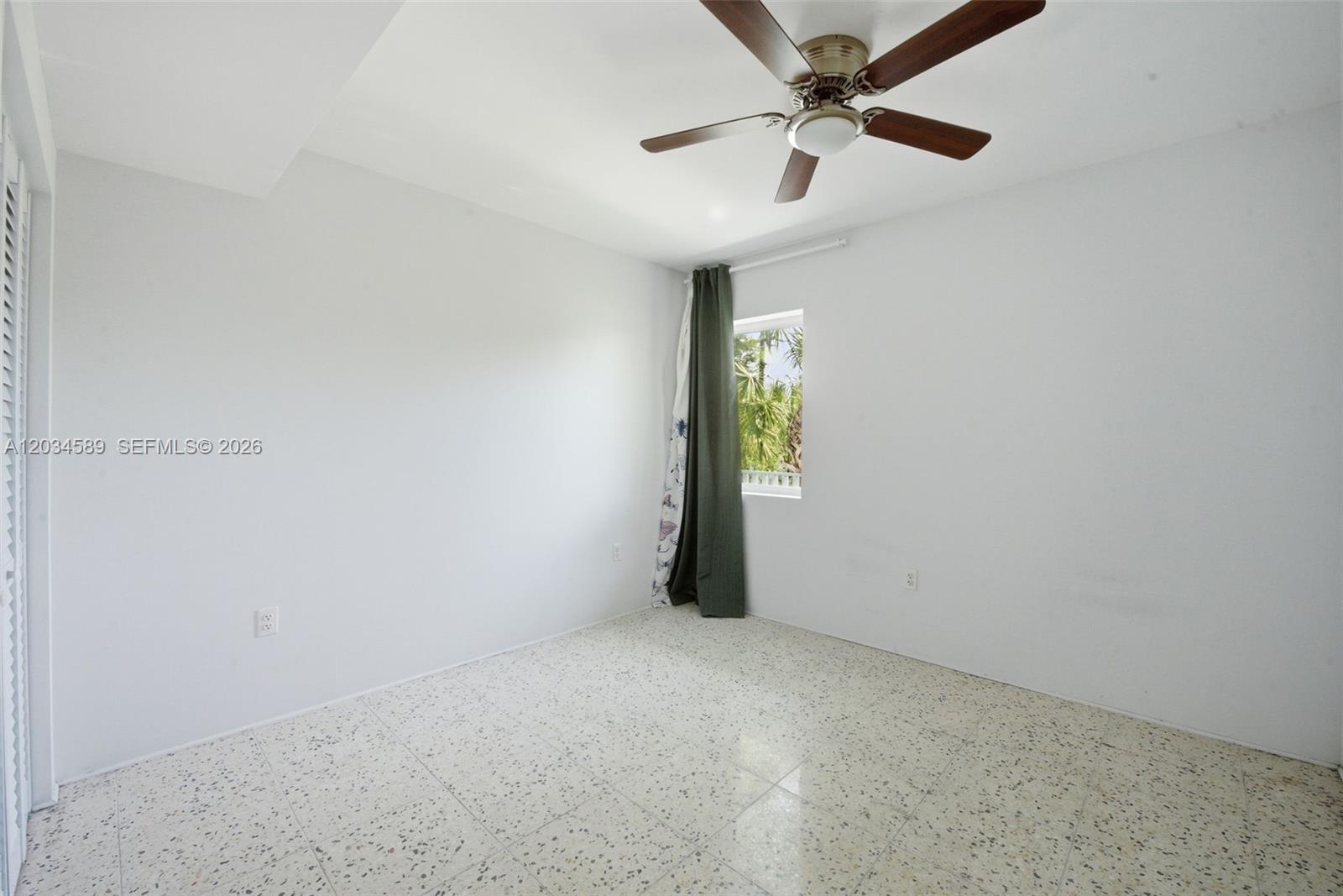 An empty room features white walls, a ceiling fan, and light-colored speckled tile flooring — 127 NW 74th St # 3, Miami FL 33150, MIAMI, FL