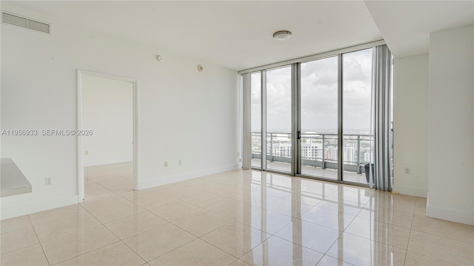 An empty living room features white walls, tile flooring, and floor-to-ceiling windows with balcony access — 90 SW 3rd St # 10, Miami FL 33130, MIAMI, FL