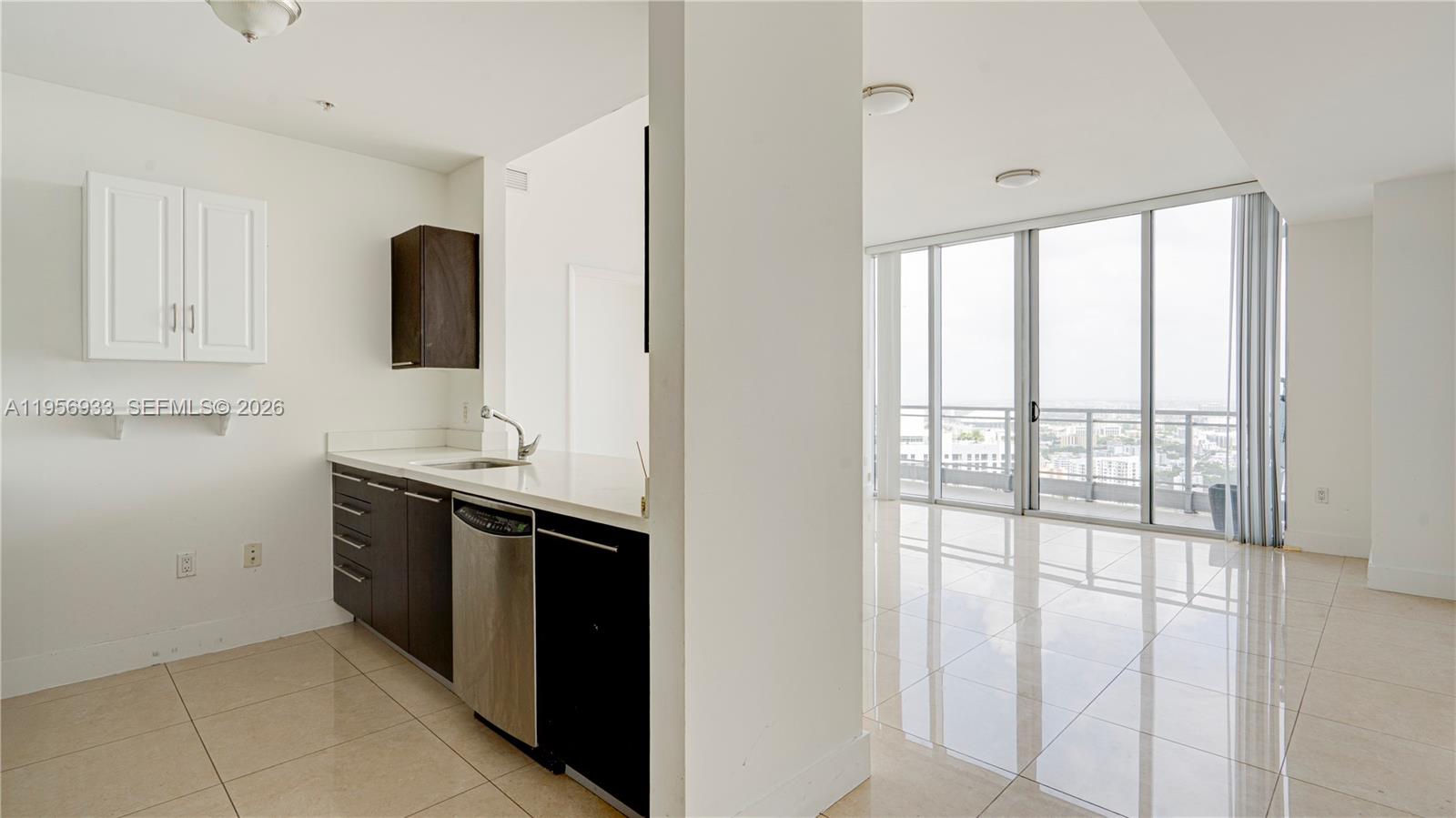 A kitchen with dark cabinets and white countertops opens into a bright, tiled living area — 90 SW 3rd St # 10, Miami FL 33130, MIAMI, FL