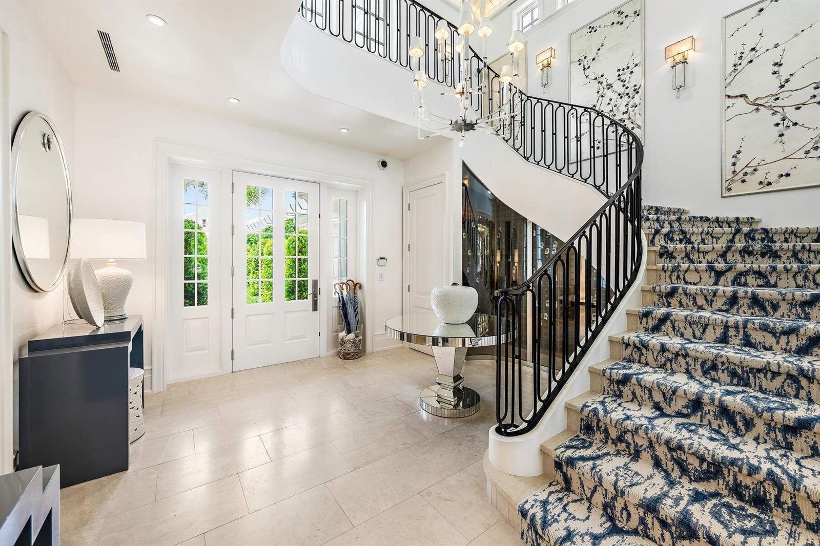 A bright foyer features a curved staircase with patterned carpet and a black iron railing — 608 Island Drive, Palm Beach FL 33480, PALM BEACH, FL