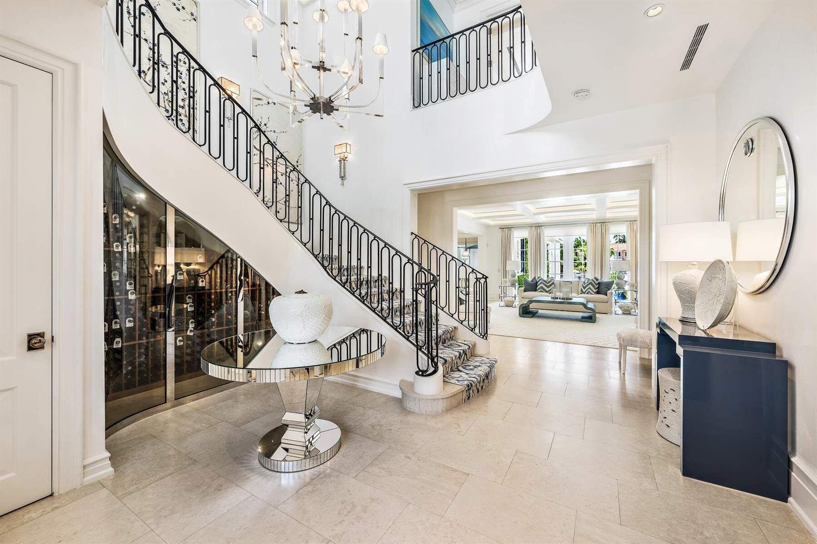 A grand foyer features a curved staircase, a glass-enclosed wine cellar, and marble flooring — 608 Island Drive, Palm Beach FL 33480, PALM BEACH, FL