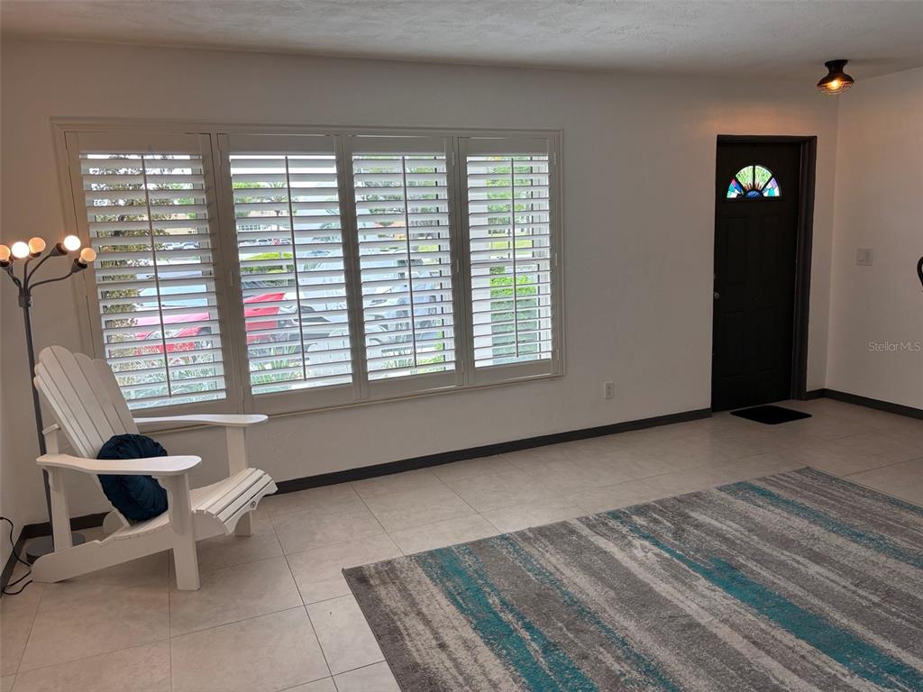 A living room features white plantation shutters, a white Adirondack chair, and a patterned rug — 2020 WORLD PARKWAY BOULEVARD UNIT 10, CLEARWATER, FL