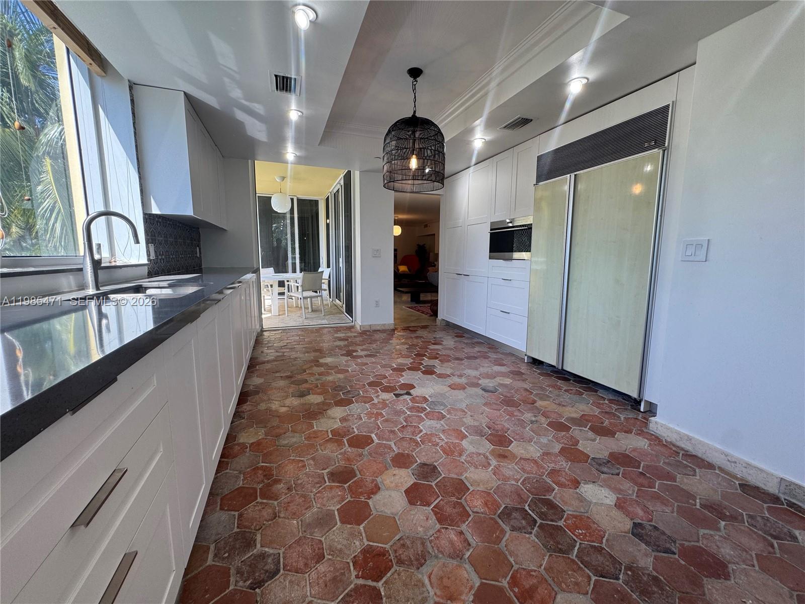 A kitchen features white cabinetry, a dark countertop, and terracotta hexagonal floor tiles — 445 Grand Bay Dr # 310, Key Biscayne FL 33149, KEY BISCAYNE, FL