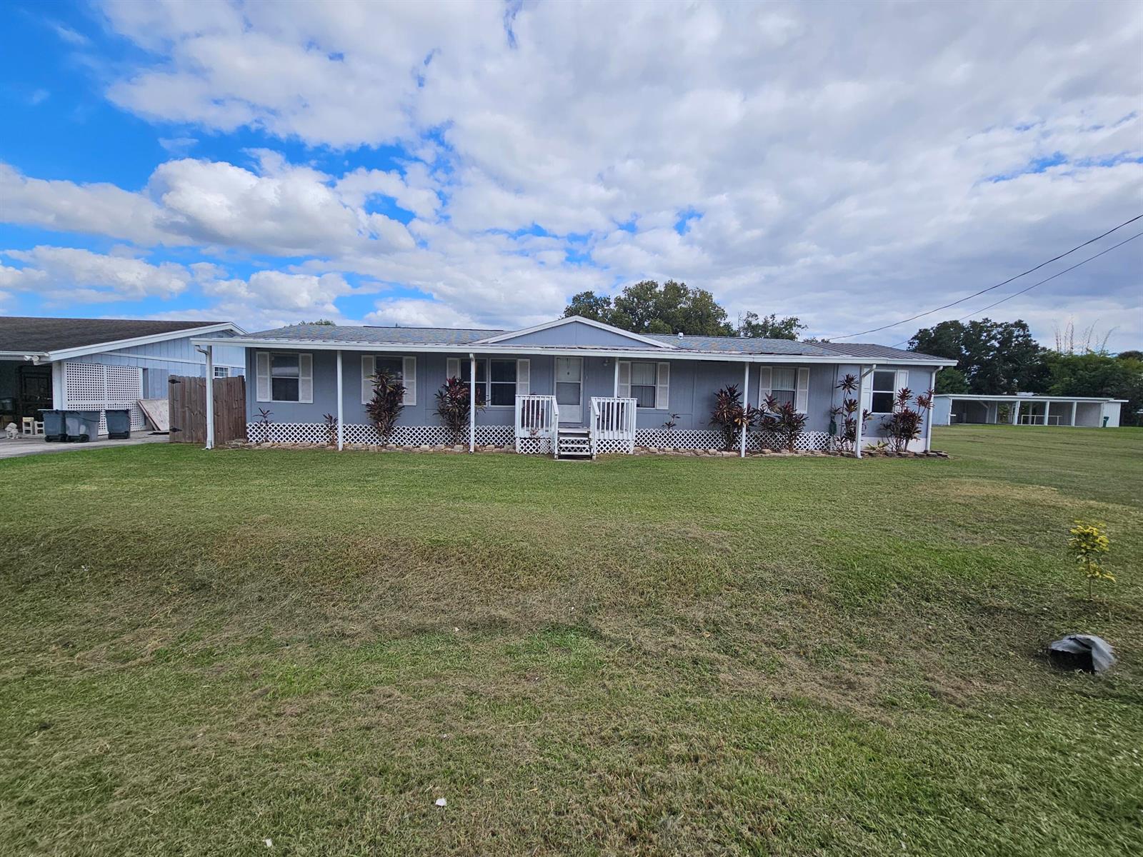 A light blue manufactured home with a front porch sits on a large grassy lot — 3222 SE 34th Avenue, Okeechobee FL 34974, OKEECHOBEE, FL
