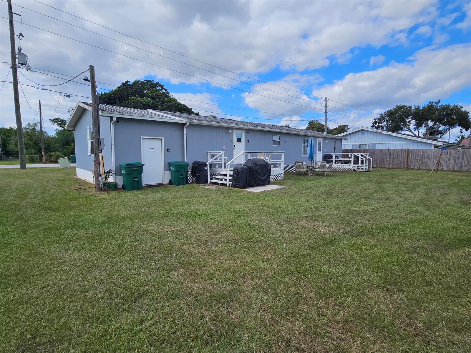 A single-story blue house with a white door, two decks, and green trash bins outside — 3222 SE 34th Avenue, Okeechobee FL 34974, OKEECHOBEE, FL