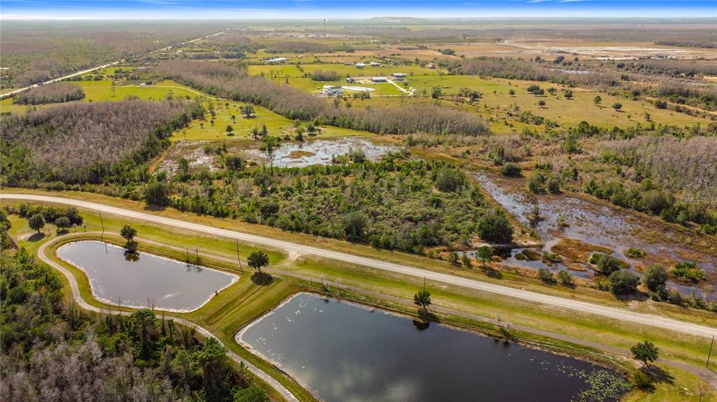An aerial view shows two ponds, a paved road, and surrounding rural land with vegetation — 0 COMMUNITY CENTER ROAD, ST CLOUD, FL