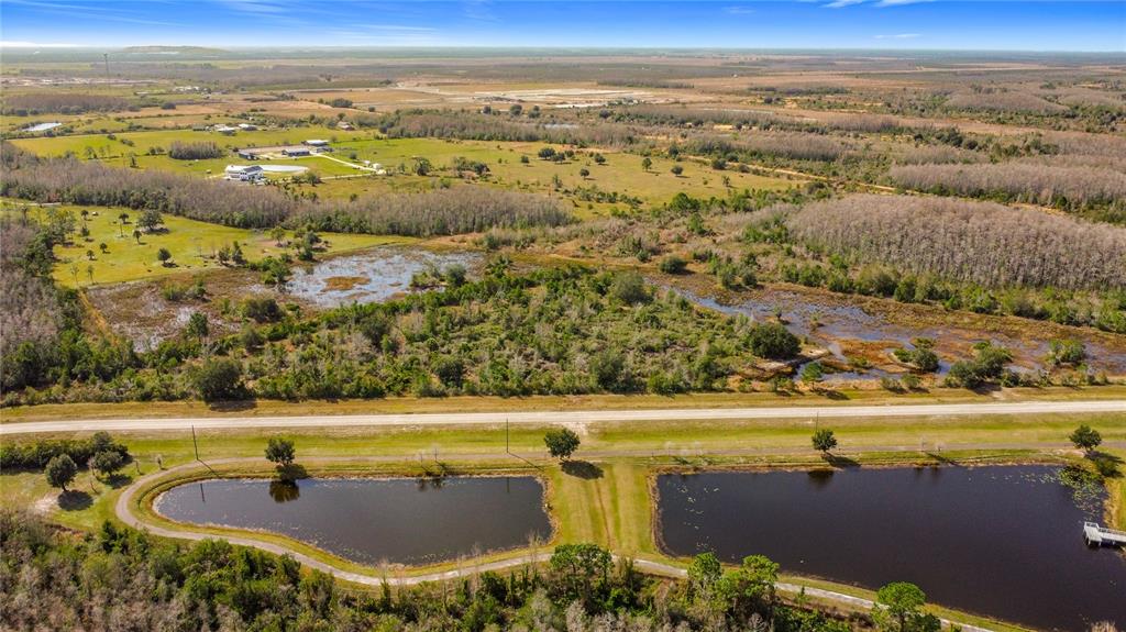 An aerial view shows a rural landscape with two ponds, a road, and wooded wetlands — 0 COMMUNITY CENTER ROAD, ST CLOUD, FL