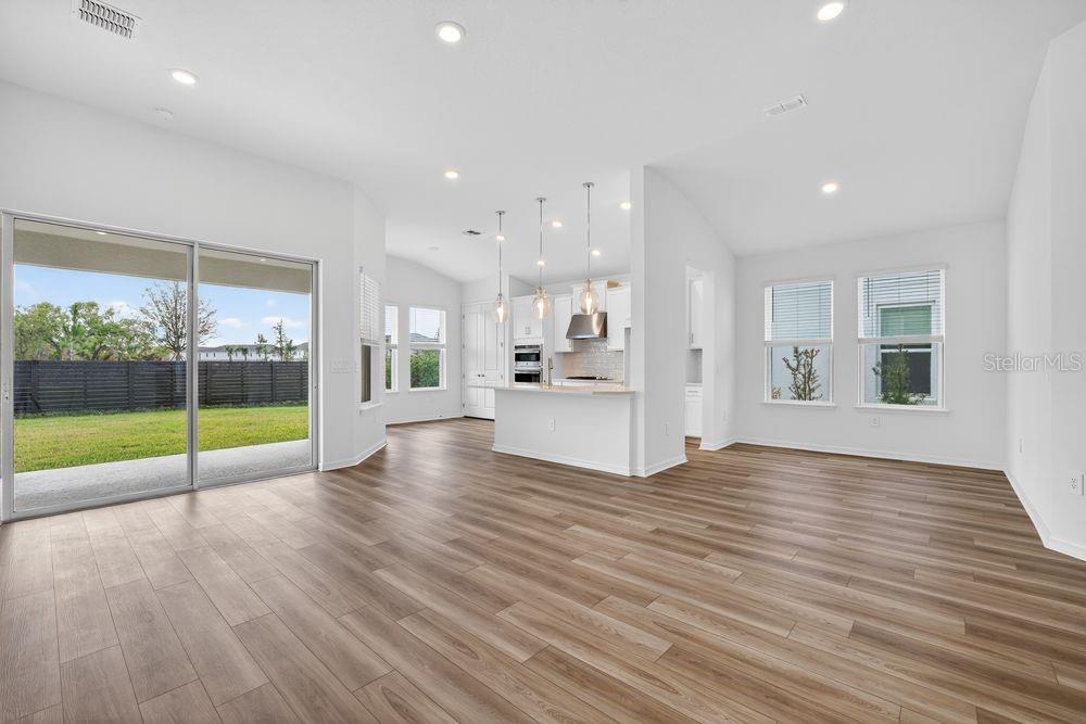 An open-concept living area with light wood-look flooring, a kitchen island, and sliding glass doors — 12743 DOCKYARD TRAIL, PALMETTO, FL
