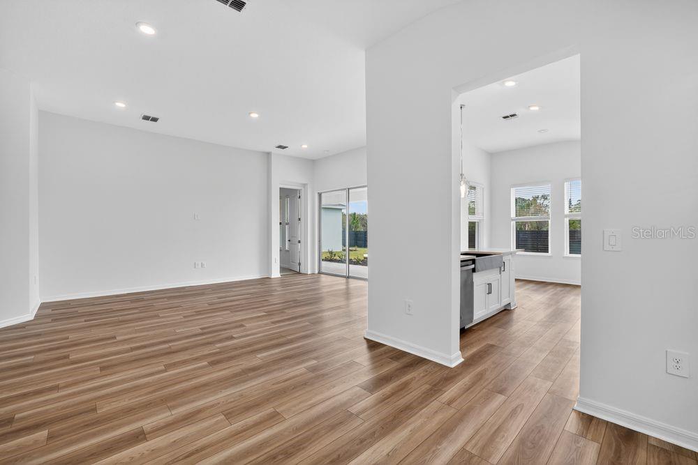An open-concept living area with light wood-look flooring and a view into the kitchen — 12743 DOCKYARD TRAIL, PALMETTO, FL