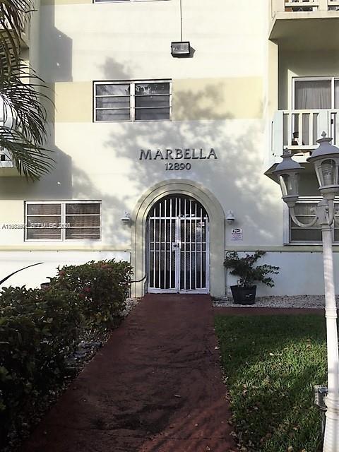 The exterior of a multi-story apartment building features a gated arched entrance and landscaping — 12890 NE 8th Ave # 101, North Miami FL 33161, NORTH MIAMI, FL
