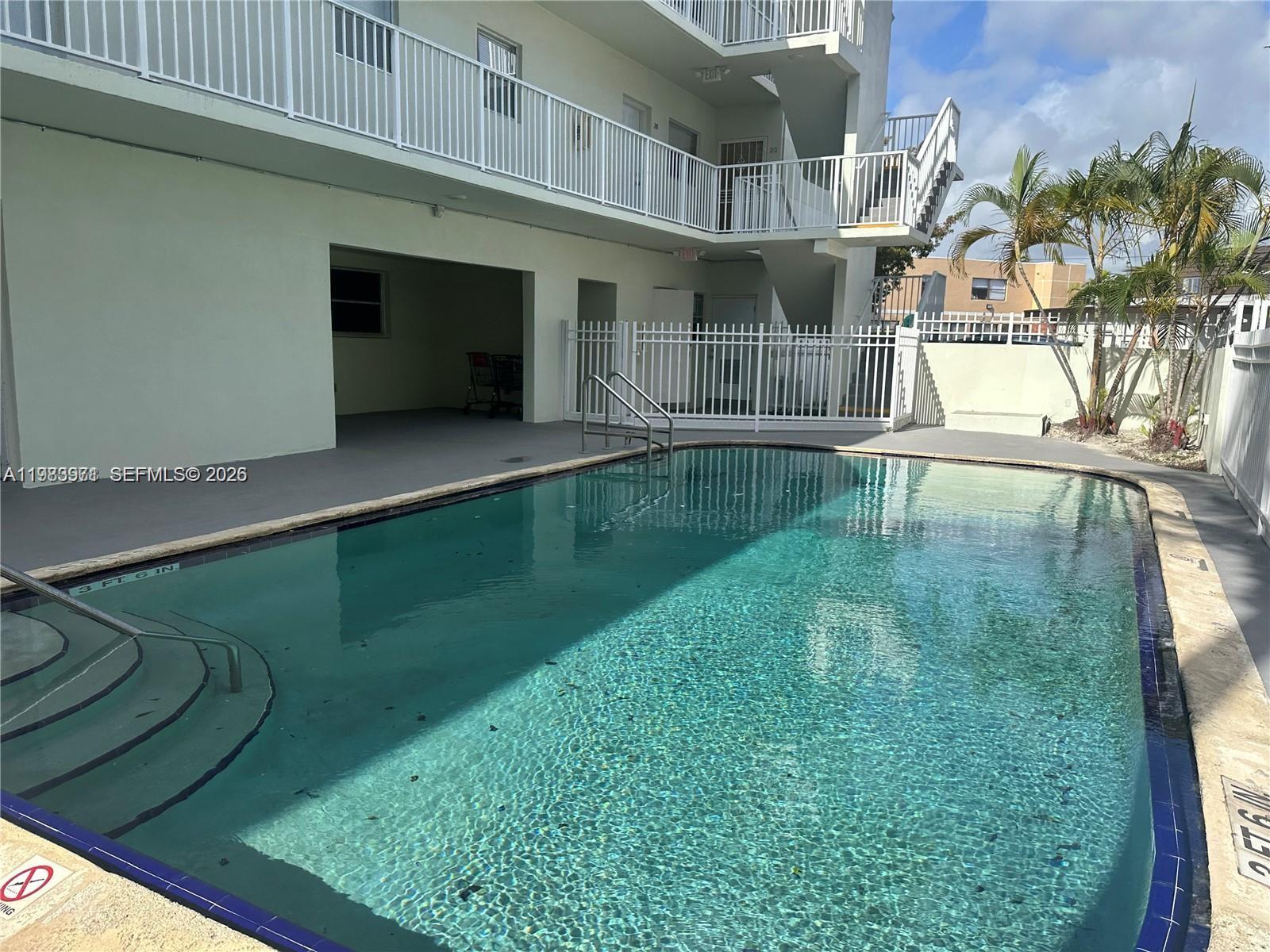 A swimming pool sits in front of a multi-story apartment building with white railings — 12890 NE 8th Ave # 101, North Miami FL 33161, NORTH MIAMI, FL