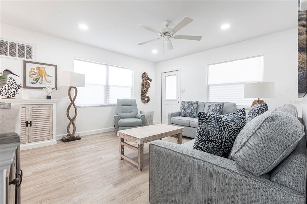 A bright living room features light wood flooring, a gray sofa, and coastal-themed decor — 6020 MIDNIGHT PASS ROAD UNIT 7, SARASOTA, FL