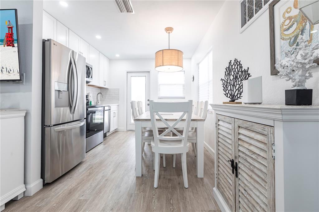 A bright kitchen and dining area features white cabinetry, stainless steel appliances, and wood-look flooring — 6020 MIDNIGHT PASS ROAD UNIT 7, SARASOTA, FL