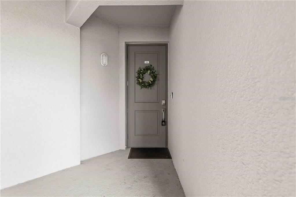 A gray front door with a wreath is set in a recessed, white-walled entryway — 12240 WELLEN GOLF STREET UNIT 208, VENICE, FL