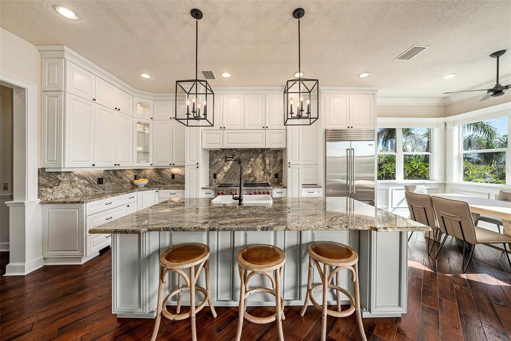 A kitchen features white cabinetry, a large granite island with three stools, and hardwood floors — 231 MIDWAY ISLAND, CLEARWATER BEACH, FL