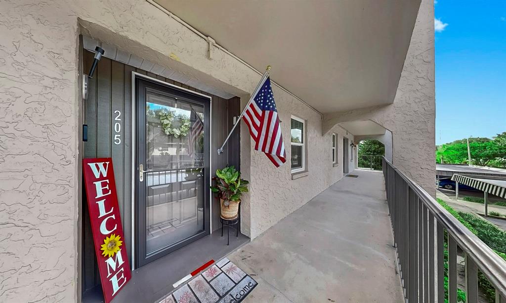 An exterior view of a residential unit entrance with a flag and welcome sign — 8799 BARDMOOR BOULEVARD UNIT 205, SEMINOLE, FL