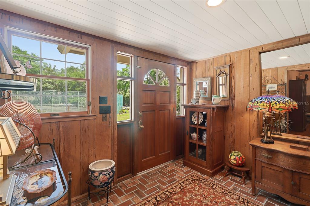 An entryway with wood-paneled walls, brick flooring, a wooden front door, and a stained-glass lamp — 6491 SPRUCE CREEK ROAD, PORT ORANGE, FL