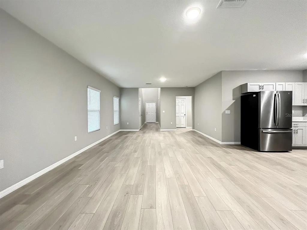 An open-concept living area features light gray walls, wood-look flooring, and a stainless steel refrigerator — 7540 FREESIA TRACE, WESLEY CHAPEL, FL