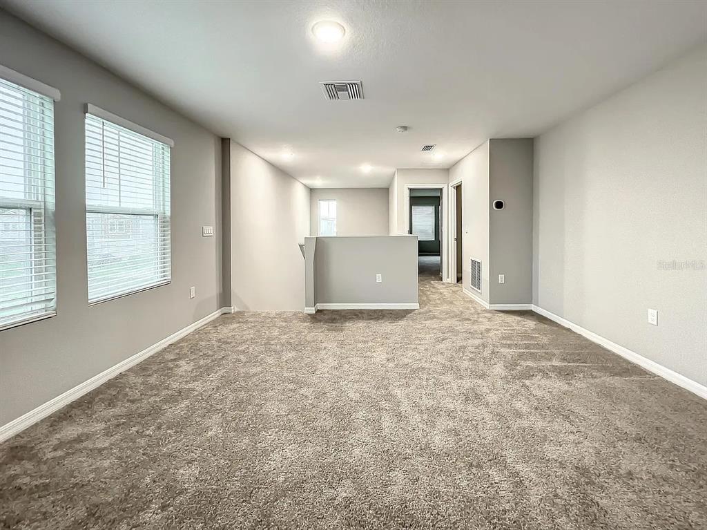 An empty carpeted room with gray walls, two windows, and a partial wall partition — 7540 FREESIA TRACE, WESLEY CHAPEL, FL