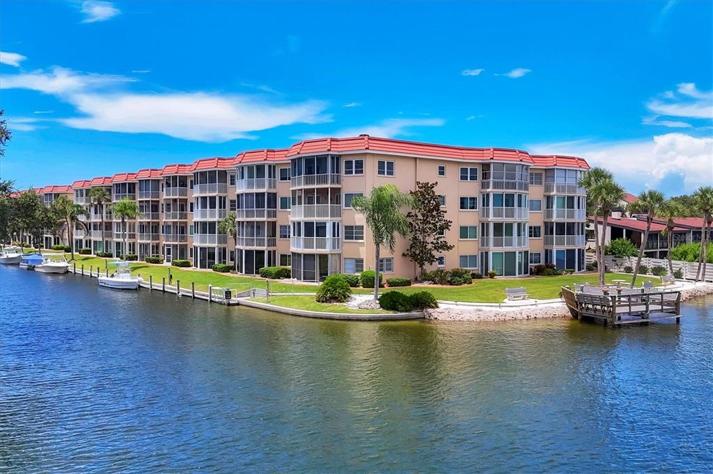 A sunroom with tile floors, two blue chairs, and a view of a canal and buildings — 1350 N PORTOFINO DRIVE UNIT 107, SARASOTA, FL