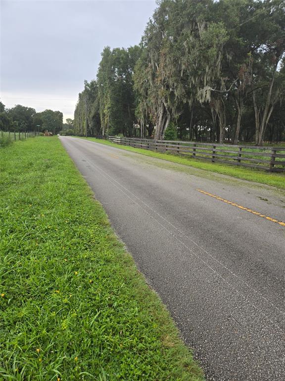 A paved road runs alongside a grassy field and a wooden fence lined with trees — 890 GRAND RONDO W, CRESCENT CITY, FL