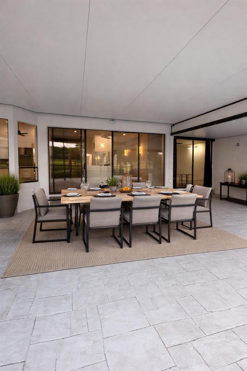 A covered outdoor patio features a large wooden dining table with eight chairs on a rug — 10106 Spyglass Way, Boca Raton FL 33498, BOCA RATON, FL