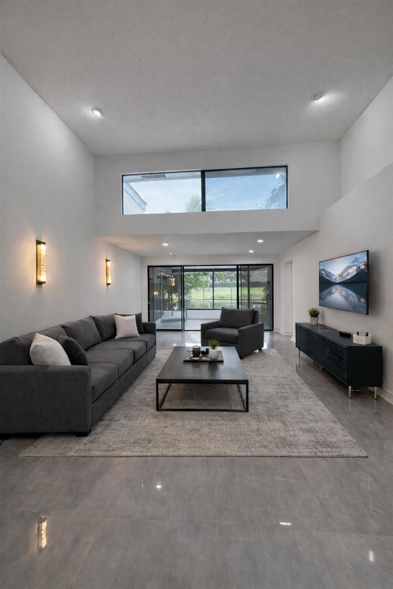 A modern living room features high ceilings, gray tile floors, a large sofa, and sliding doors — 10106 Spyglass Way, Boca Raton FL 33498, BOCA RATON, FL