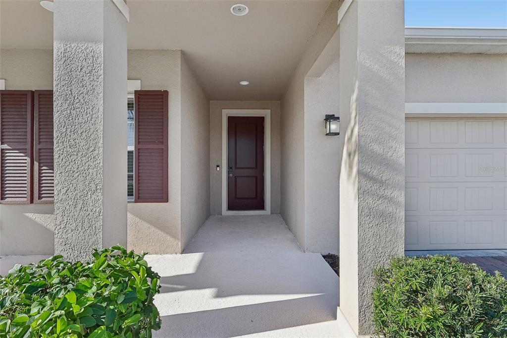 A covered entryway features a dark brown front door, beige stucco walls, and two pillars — 5585 VIGO LOOP, ST CLOUD, FL