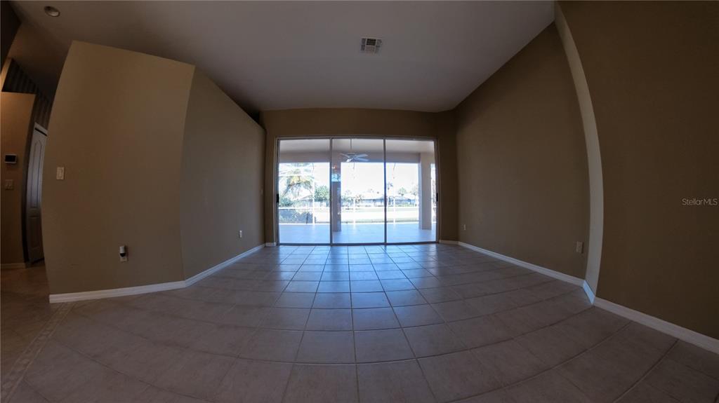 A room with tan walls and tiled floors leads to a sliding glass door overlooking water — 11837 GRAND ISLES LANE, FORT MYERS, FL