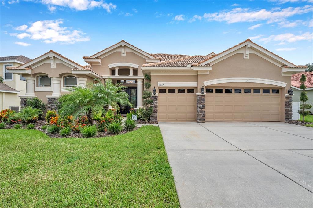 A single-story tan stucco house with a three-car garage and a landscaped front yard — 11519 BELLE HAVEN DRIVE, NEW PORT RICHEY, FL