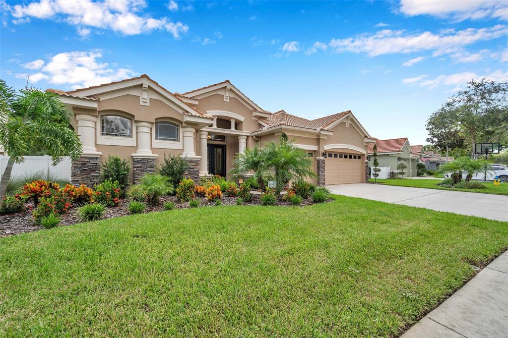 A single-story tan stucco house with a tile roof, stone accents, and a front lawn — 11519 BELLE HAVEN DRIVE, NEW PORT RICHEY, FL