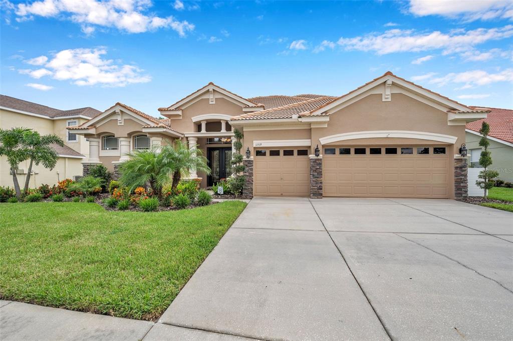 A single-story tan stucco house with a tile roof, three-car garage, and front landscaping — 11519 BELLE HAVEN DRIVE, NEW PORT RICHEY, FL