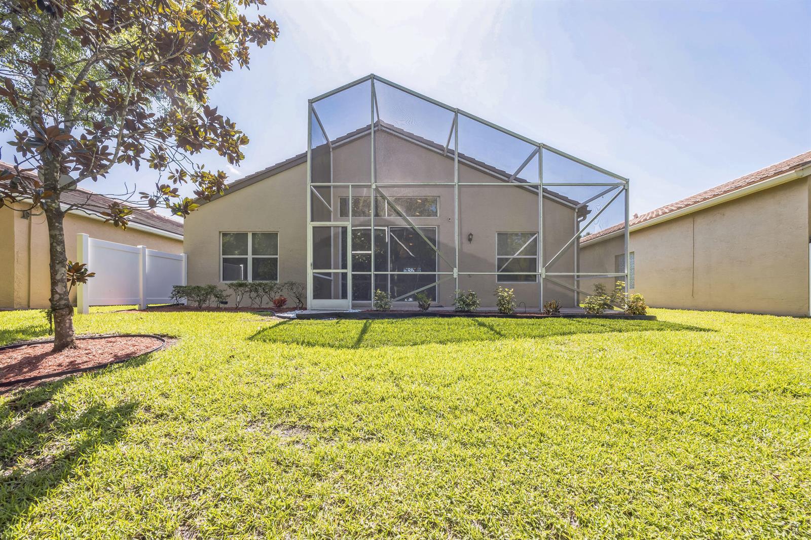 The rear exterior of a house features a screened-in patio and a grassy lawn — 5780 Saddle Trail Lane, Lake Worth FL 33449, LAKE WORTH, FL