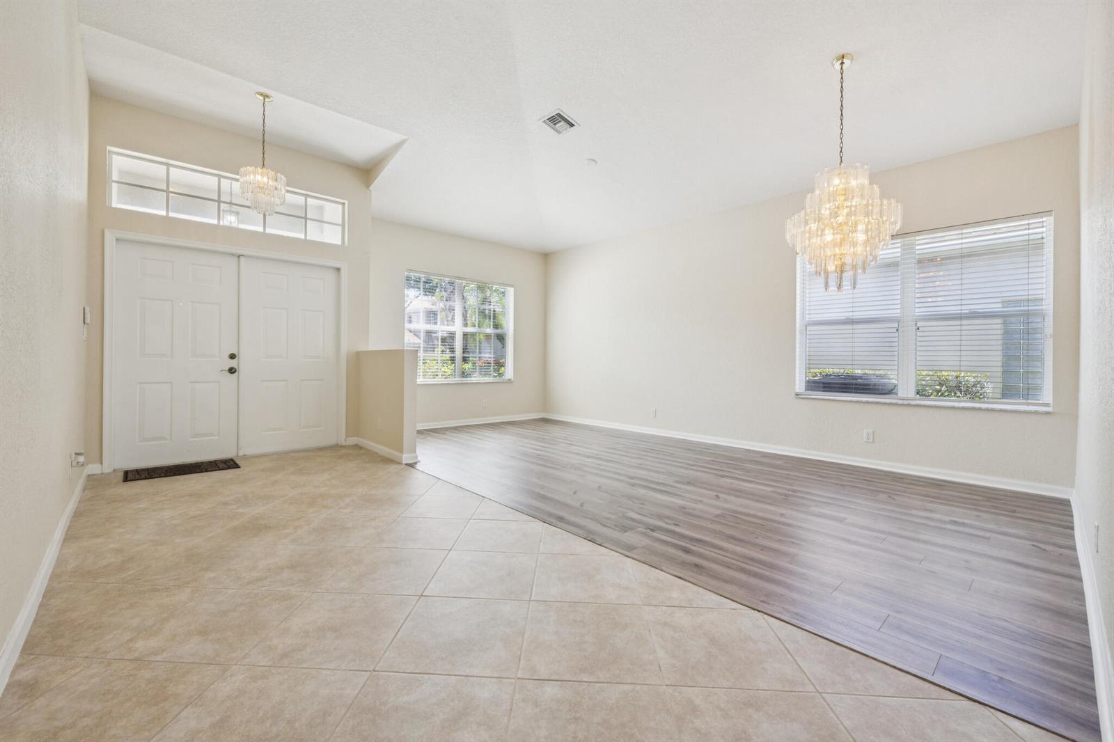 A bright living area features a mix of tile and wood-look flooring with two chandeliers — 5780 Saddle Trail Lane, Lake Worth FL 33449, LAKE WORTH, FL
