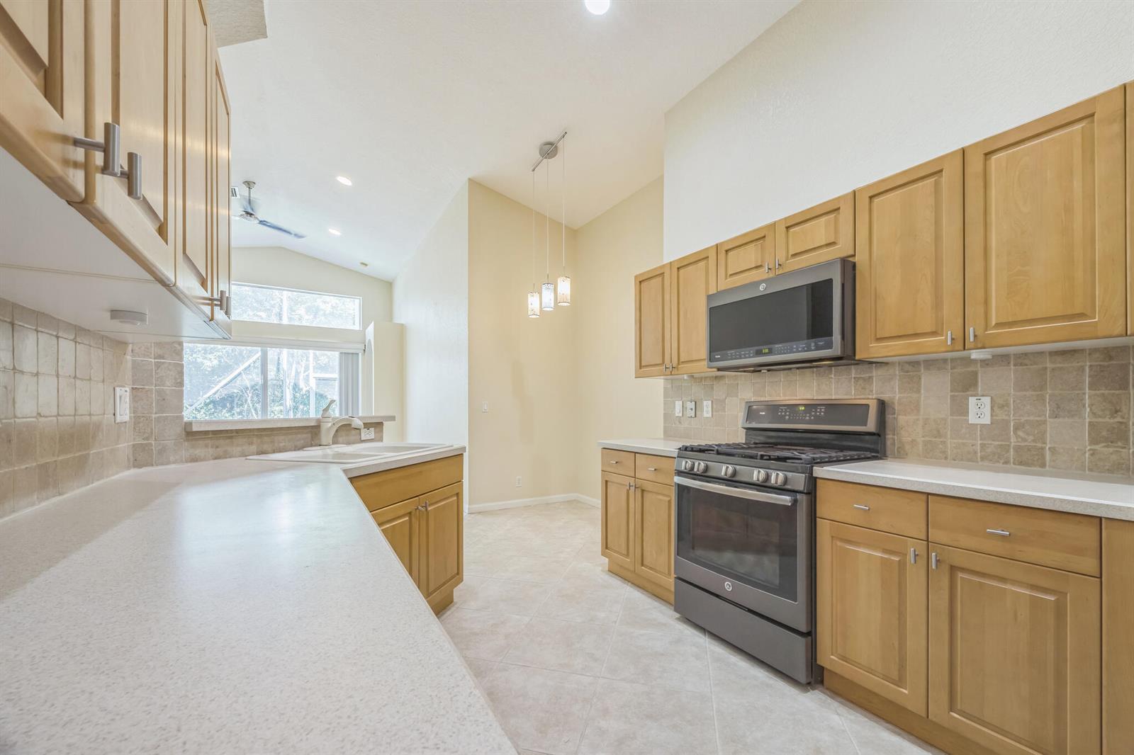 A kitchen features light wood cabinets, a stainless steel range, and a tiled backsplash — 5780 Saddle Trail Lane, Lake Worth FL 33449, LAKE WORTH, FL