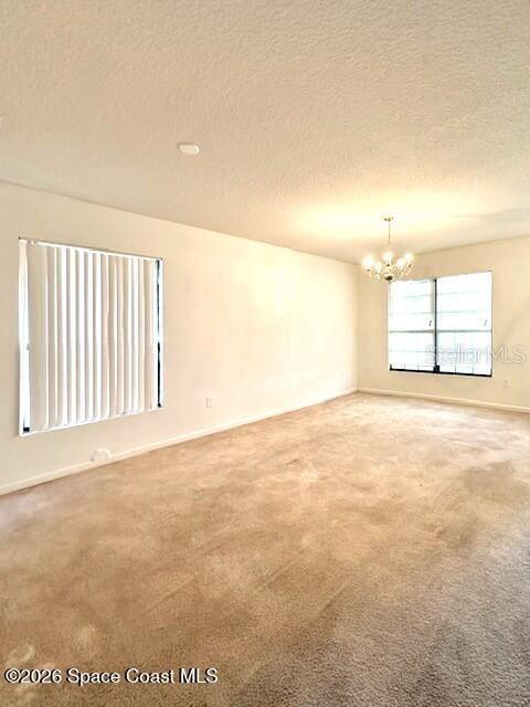 An empty room features beige carpeting, white walls, a chandelier, and two windows with blinds — 782 MARIAN COURT, TITUSVILLE, FL