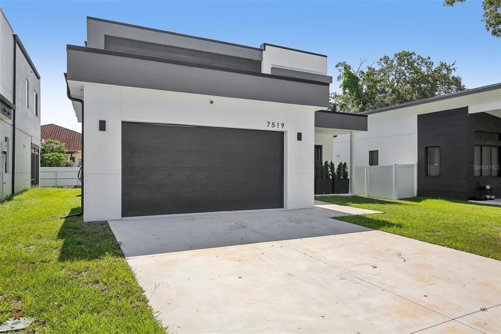 A modern, single-story house exterior features a dark garage door and white stucco walls — 7519 N COOLIDGE AVENUE, TAMPA, FL