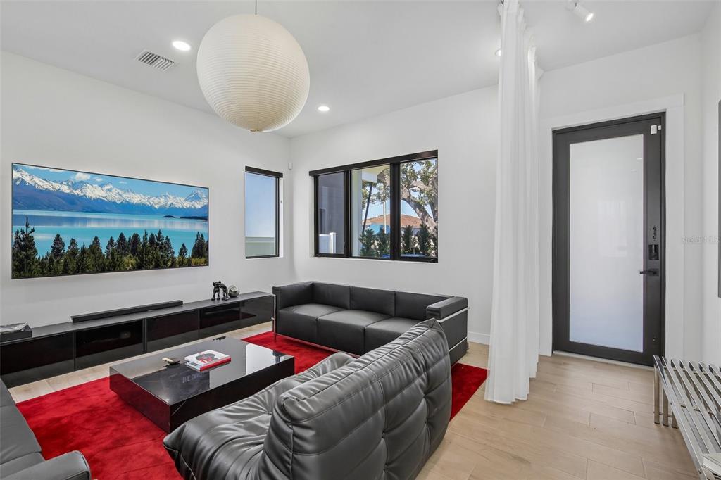 A modern living room features black leather sofas, a red area rug, and a large television — 7519 N COOLIDGE AVENUE, TAMPA, FL