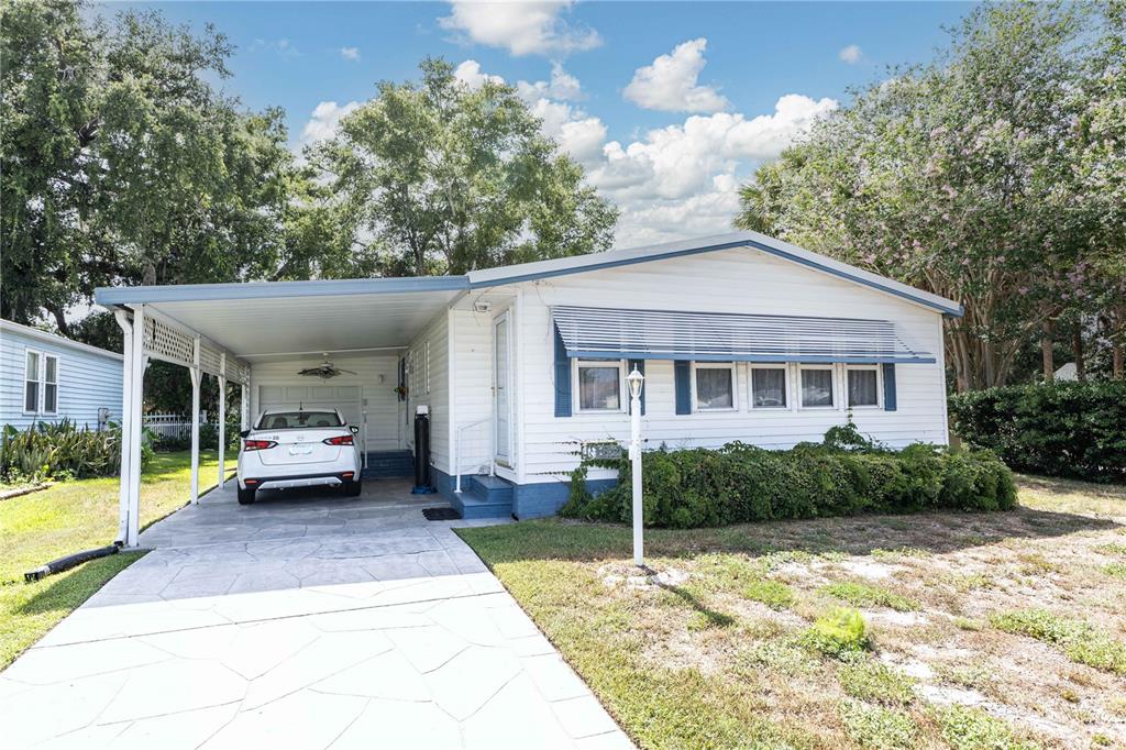 A white single-story manufactured home features a carport, a paved driveway, and blue trim — 1159 PARADISE DRIVE, LADY LAKE, FL